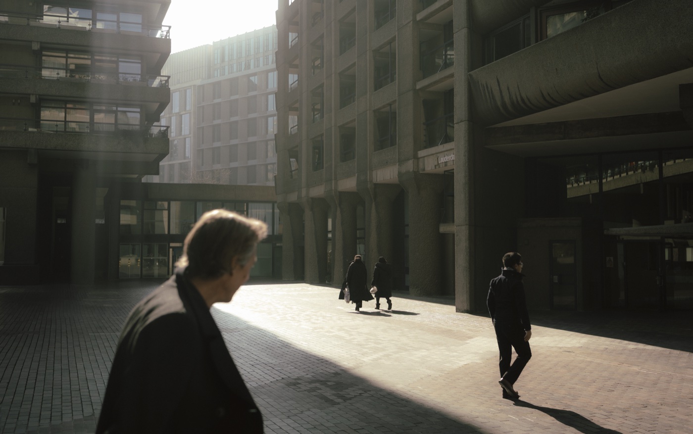 Three strangers crossing a backlit courtyard, each on their own line