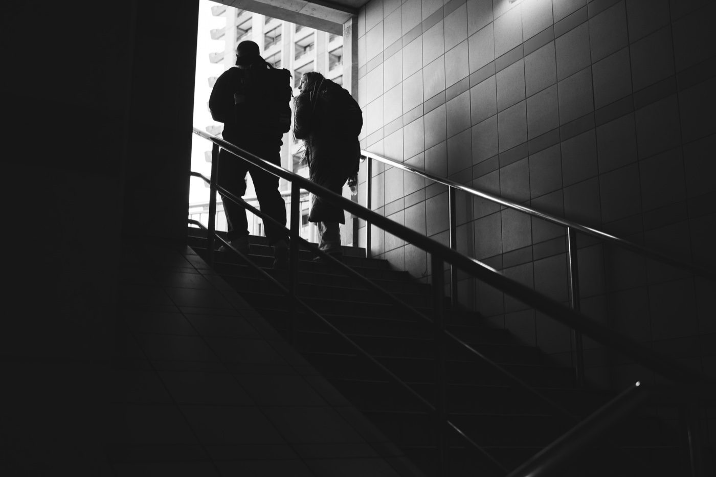 Two figures climbing a darkened staircase toward a single lit opening